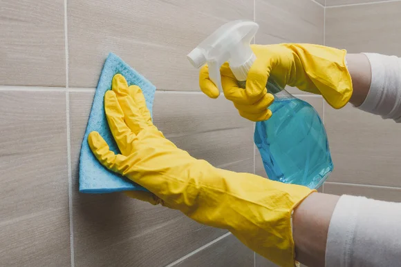 Person reinigt Fliesen mit Spray und Lappen.